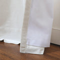 Detailed shot of white and off-white fabrics with a prominent velvet trim and subtle stitching pooled on a polished brown wooden floor