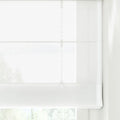 Photograph of a sheer white Roman blind covering a window, detailed with distinct horizontal folds, a visible lift cord mechanism, and softly filtered light revealing blurred green foliage outside