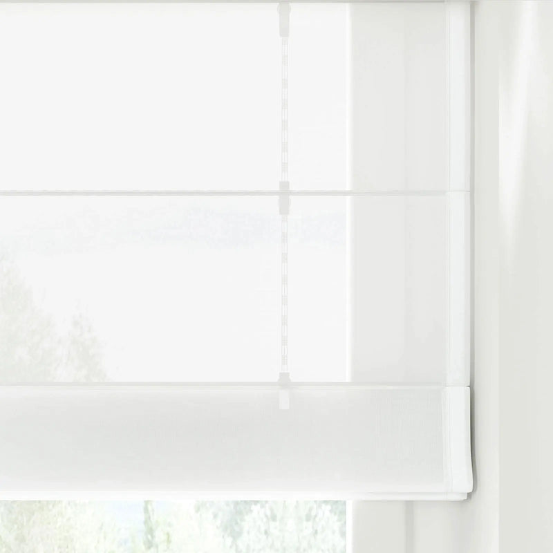 Photograph of a sheer white Roman blind covering a window, detailed with distinct horizontal folds, a visible lift cord mechanism, and softly filtered light revealing blurred green foliage outside