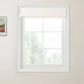 Van Gogh print of a rural landscape framed on a light beige wall next to a white multi-pane window with a textured white Roman blind revealing blurred green foliage outside