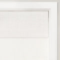 Photograph of a light beige textured linen-look roman shade partially drawn in a crisp white window frame