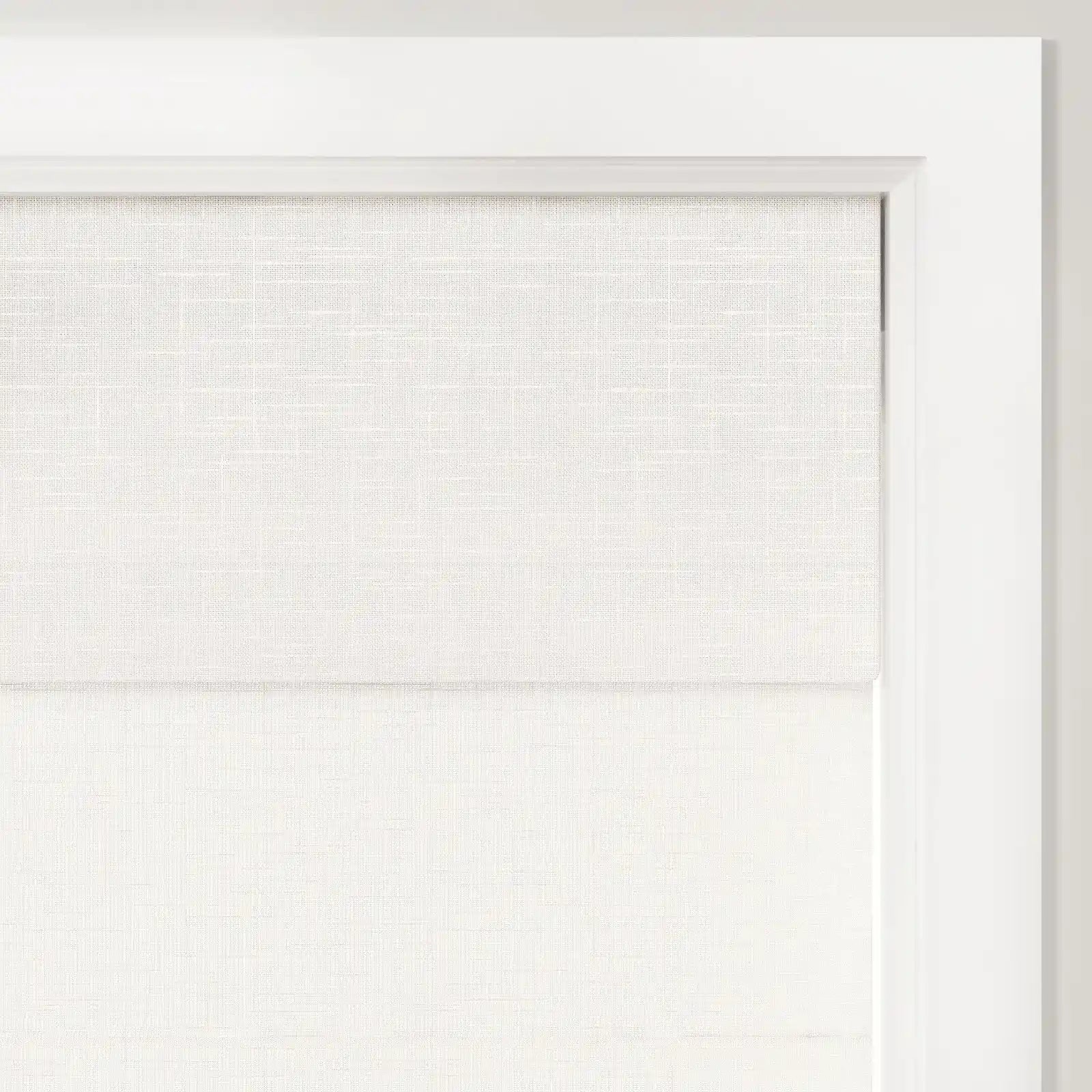 Photograph of a light beige textured linen-look roman shade partially drawn in a crisp white window frame