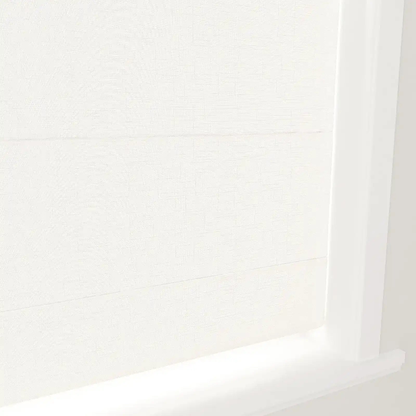 A close-up of off-white textured fabric window blinds featuring horizontal folds and a crisp white frame in a brightly lit interior