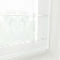 Photograph of a window with white sheer Roman blinds displaying blurred green foliage outdoors, featuring subtle vertical striped cords and bright diffused natural light creating a minimalist ambiance