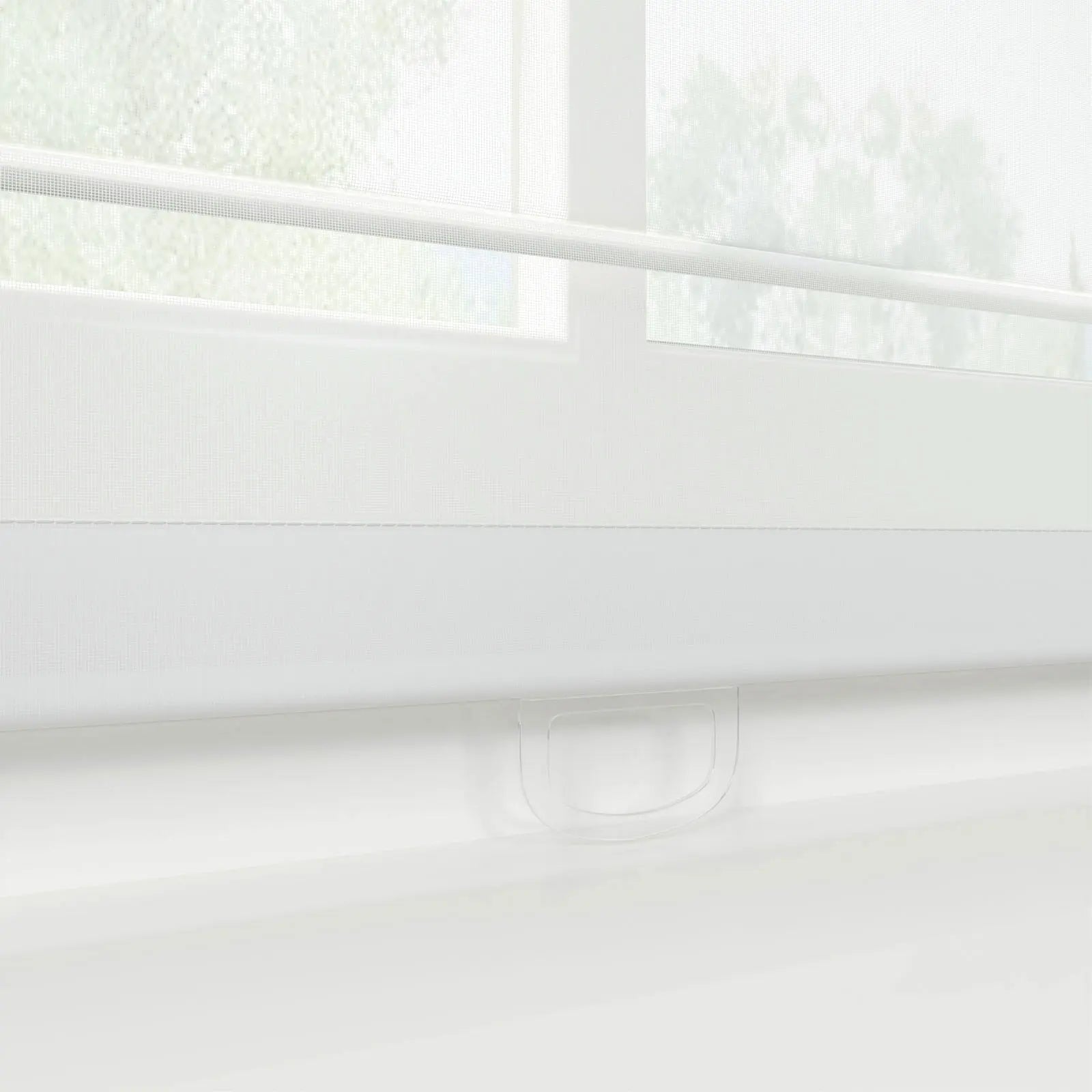 Photograph of a modern white day-night roller blind featuring alternating sheer and opaque horizontal fabric strips, a translucent plastic pull handle at the bottom, and blurred green foliage visible through the window