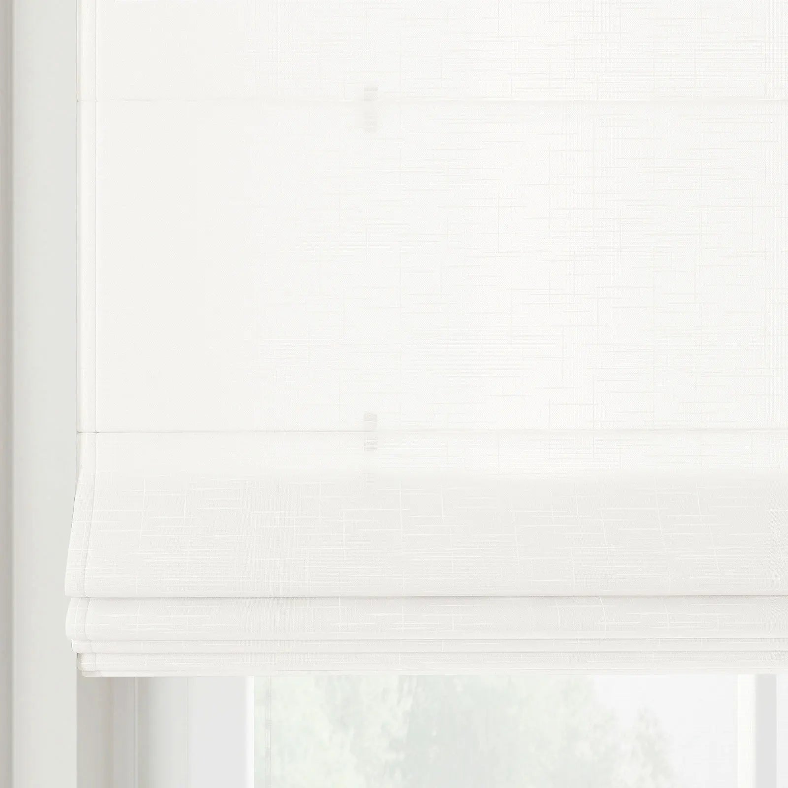 A white textured roman blind is neatly folded in layers, partially obscuring a window with soft diffused light behind it