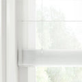 Modern white sheer Roman blind with a subtle grid texture covering a window, with a faint cord mechanism visible and blurred green foliage outside