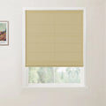Textile Roman blind in light beige featuring neat horizontal folds on a white window frame, revealing a blurred green outdoor scene, with a framed colorful Van Gogh landscape print visible on the adjacent wall
