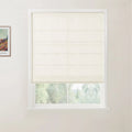 A photograph showcasing a window with a cream textured Roman blind featuring horizontal folds, set in a white frame, overlooking a blurred green landscape, with a framed Van Gogh print on the left wall