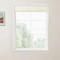 Photograph of a bright room featuring a white-framed window with a cream Roman shade, overlooking blurred green trees, with a framed Van Gogh print visible on the light beige wall
