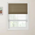 A framed Van Gogh print and a window with a dark brown Roman blind and white sheer blind on a cream wall