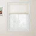 Photograph of a modern interior featuring a cream Roman blind half-closed over a white grid window looking out to blurred green trees, with a framed Van Gogh landscape print on the pale beige wall