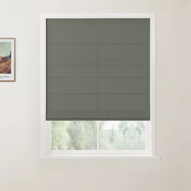 A modern interior features a textured grey-green Roman blind covering a white-framed window with blurred green foliage outside and a framed Van Gogh print on the adjacent wall
