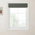 Photograph of an interior window featuring a dark green textured Roman blind above a white multi-pane window frame looking out to a hazy green natural landscape, with a framed Van Gogh print depicting colorful fields on the adjacent light beige wall