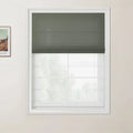 A white framed window with a dark green textured Roman blind partially lowered over a bright view of outdoor trees with a framed Van Gogh print visible on the light beige wall