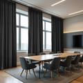 A modern conference room featuring floor-to-ceiling dark grey curtains, a long light wood table surrounded by ergonomic grey chairs, and a large wall-mounted TV with warm LED accent lighting