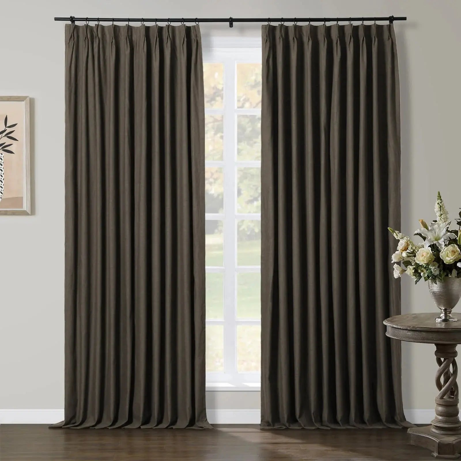 Two dark brown pleated window curtains in a modern room with a white-framed window, a minimalist botanical print, and an ornate twisted-base table with white and cream flowers