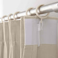 Beige pleated curtains with a linen-like texture hanging from a silver rod with white plastic rings and a visible white non-woven reinforcing strip
