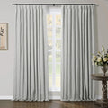 Light gray pleated curtains on a black rod in a room with dark wood floors and a visible window, complemented by a carved side table with a bouquet of white and yellow flowers and framed abstract plant art