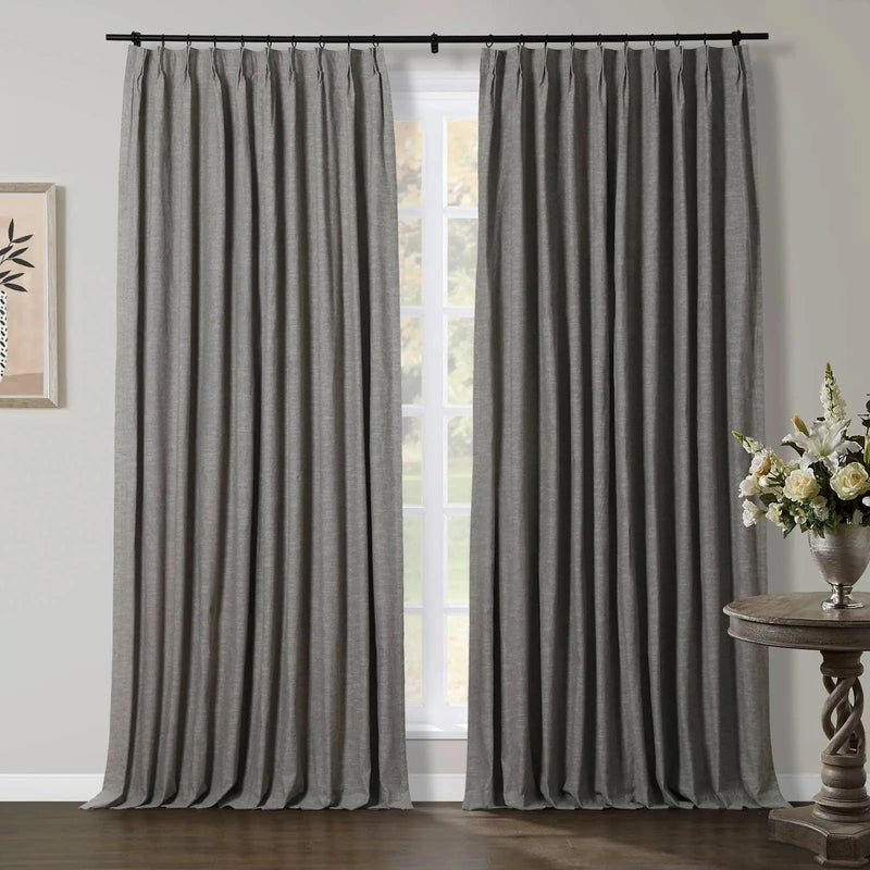 Grey pleated curtains hang from a black rod over a window, flanked by abstract wall art and a silver vase with a white floral arrangement on a carved wooden table