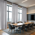 A contemporary conference room featuring floor-to-ceiling light grey curtains, a long natural wood conference table with dark grey ergonomic chairs, and a wall-mounted TV with accent lighting on a dark grey wall