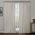 Photograph of cream-colored pinch-pleat blackout curtains on a black rod flanking a bright window revealing outdoor greenery, with a decorative wooden cabinet and botanical framed art contributing to a serene room aesthetic