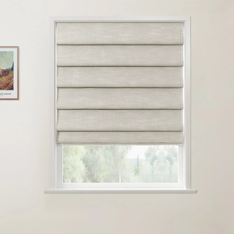 Photograph of a white-framed window featuring a beige textured Roman blind partially open to a blurred green outdoor view, positioned next to a framed Van Gogh landscape print