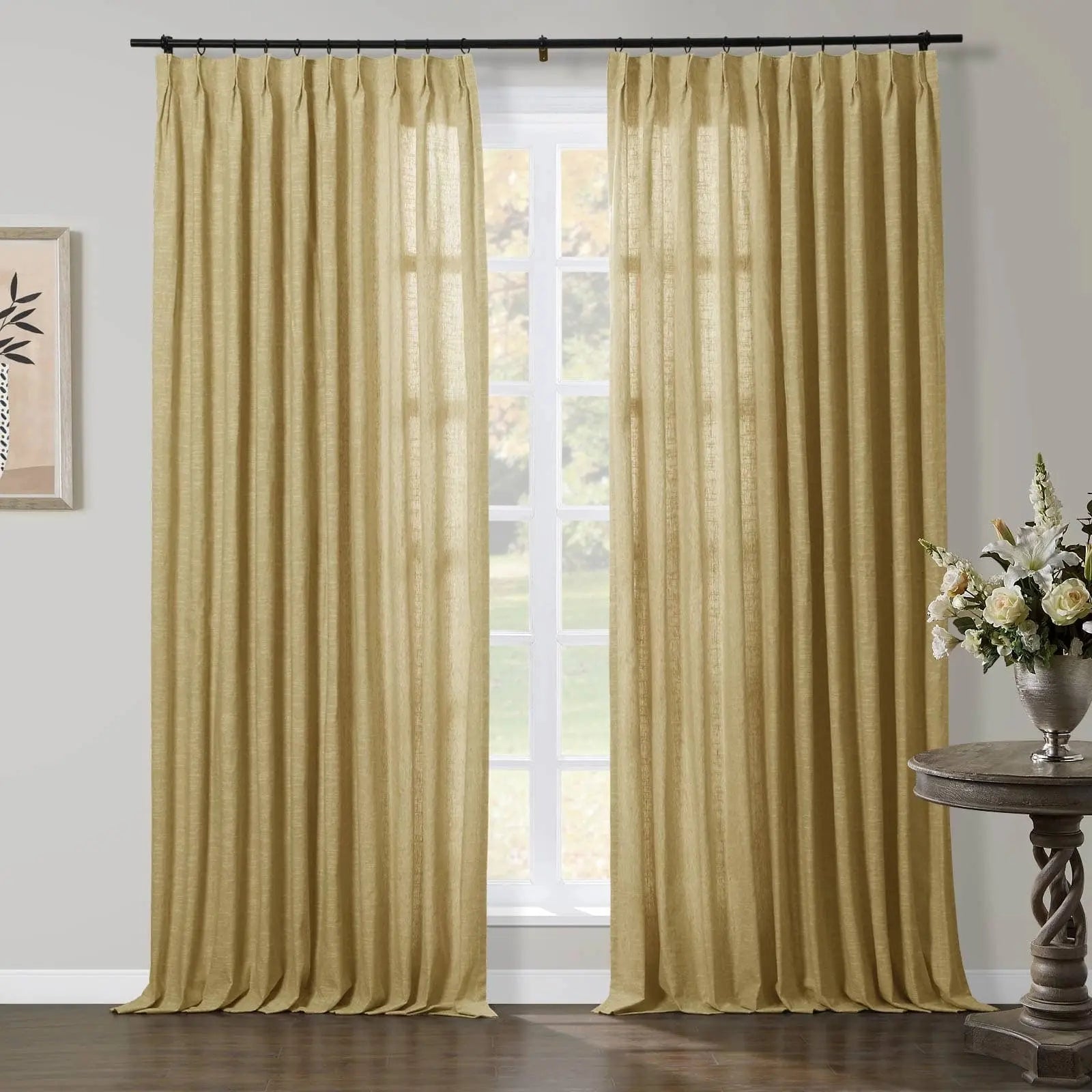 A pair of pleated, textured gold curtains framing a sunlit window in a living room, accompanied by a rustic carved wood side table adorned with white roses and lilies in a silver vase, and a framed abstract artwork on the left wall