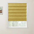 Photograph of a mustard yellow Roman blind in a white window frame, partially raised to reveal green trees outside, with a framed Van Gogh print on the left wall
