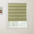 Light green textured fabric roman blind partially covering a white window frame revealing blurry trees, with a framed Van Gogh art print on the wall