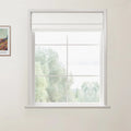 Photograph of a white-framed window with a partially lowered white Roman blind and grid panes, offering a soft view of blurred green trees, next to a framed Van Gogh print on a white wall