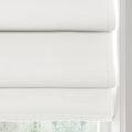 White textured Roman blinds featuring three clean horizontal folds partially covering a window, softly lit by natural light with a hint of blurred green trees beyond