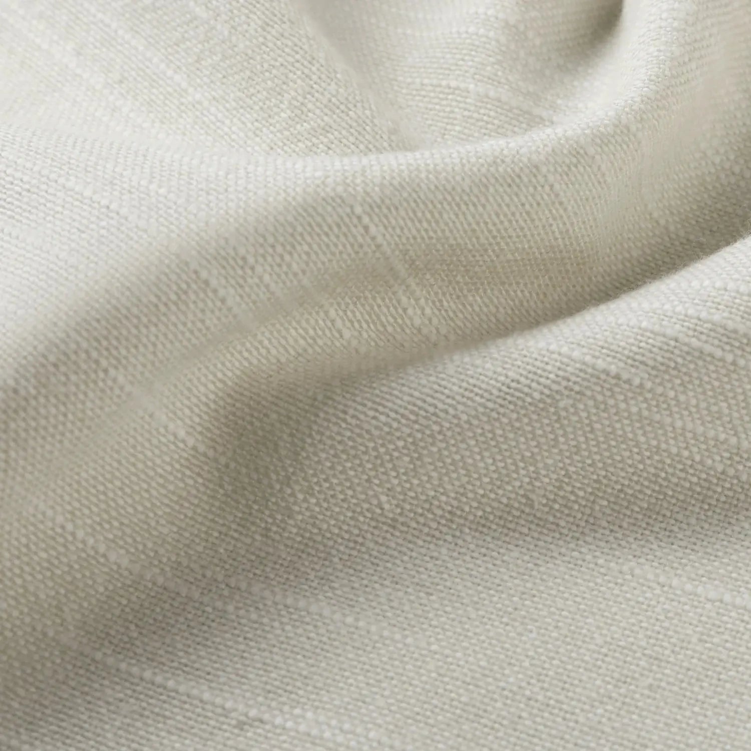 Close-up of light beige natural textured fabric displaying soft undulating folds and a visible intricate weave pattern