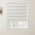 Photograph of a white textured Roman blind partially lowered in a window, with a view of green trees outside and a framed Van Gogh print on the left wall