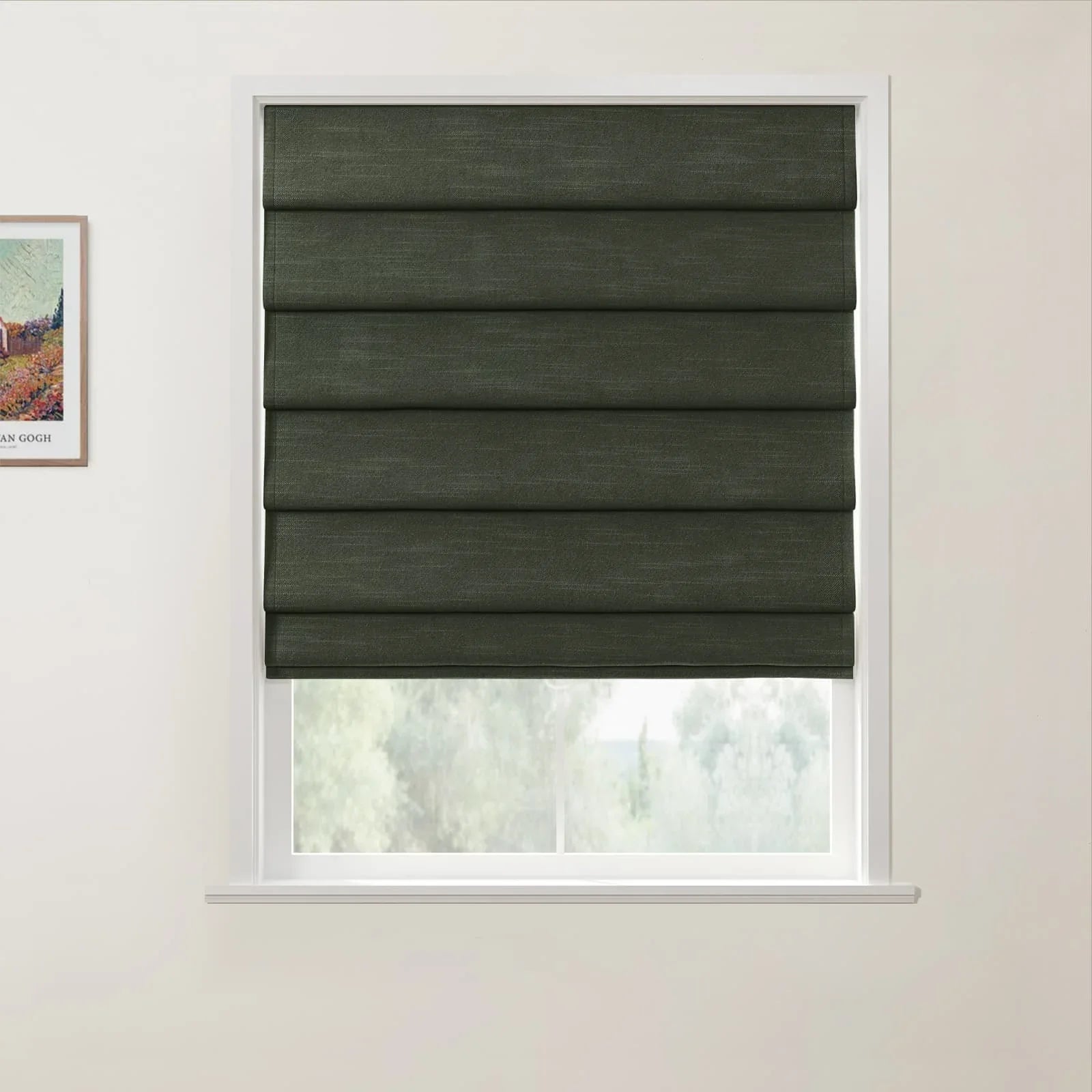 Textile Roman blind in dark green textured fabric partially lowered over a window with a blurred green outdoor view, next to a framed Vincent van Gogh landscape print on a white wall