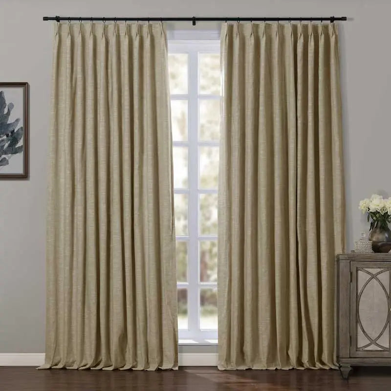 Beige linen-look pleated curtains on a black rod in an interior room with a framed blue abstract artwork on the left and a gray distressed cabinet with geometric mirrored doors topped with white flowers on the right