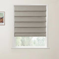 Print of Van Gogh's colorful landscape painting hanging next to a window with a textured beige Roman blind partially open, revealing blurred soft green foliage outside against a light gray wall