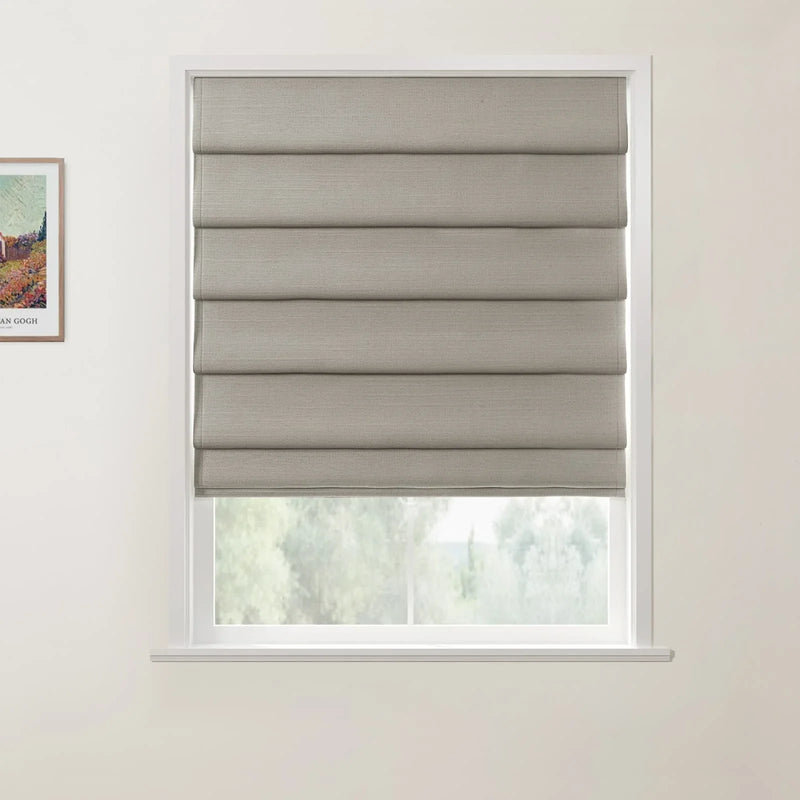 Print of Van Gogh's colorful landscape painting hanging next to a window with a textured beige Roman blind partially open, revealing blurred soft green foliage outside against a light gray wall