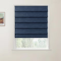 Photograph showing a dark blue textured Roman blind over a white-framed window, with blurred green foliage visible below and a partial framed Van Gogh landscape print on the adjacent light wall