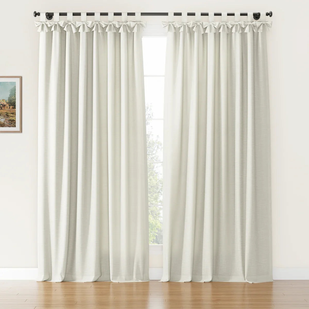 Photograph of off-white linen-look curtains with decorative tab-top bows on a black rod over a window in a bright room with hardwood floors and a framed landscape painting