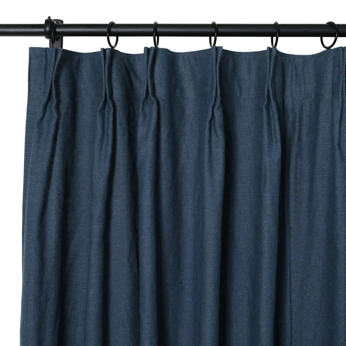 Navy blue linen-look curtain with pinch pleats suspended from a black metal rod with rings displaying subtle woven texture and rich vertical folds