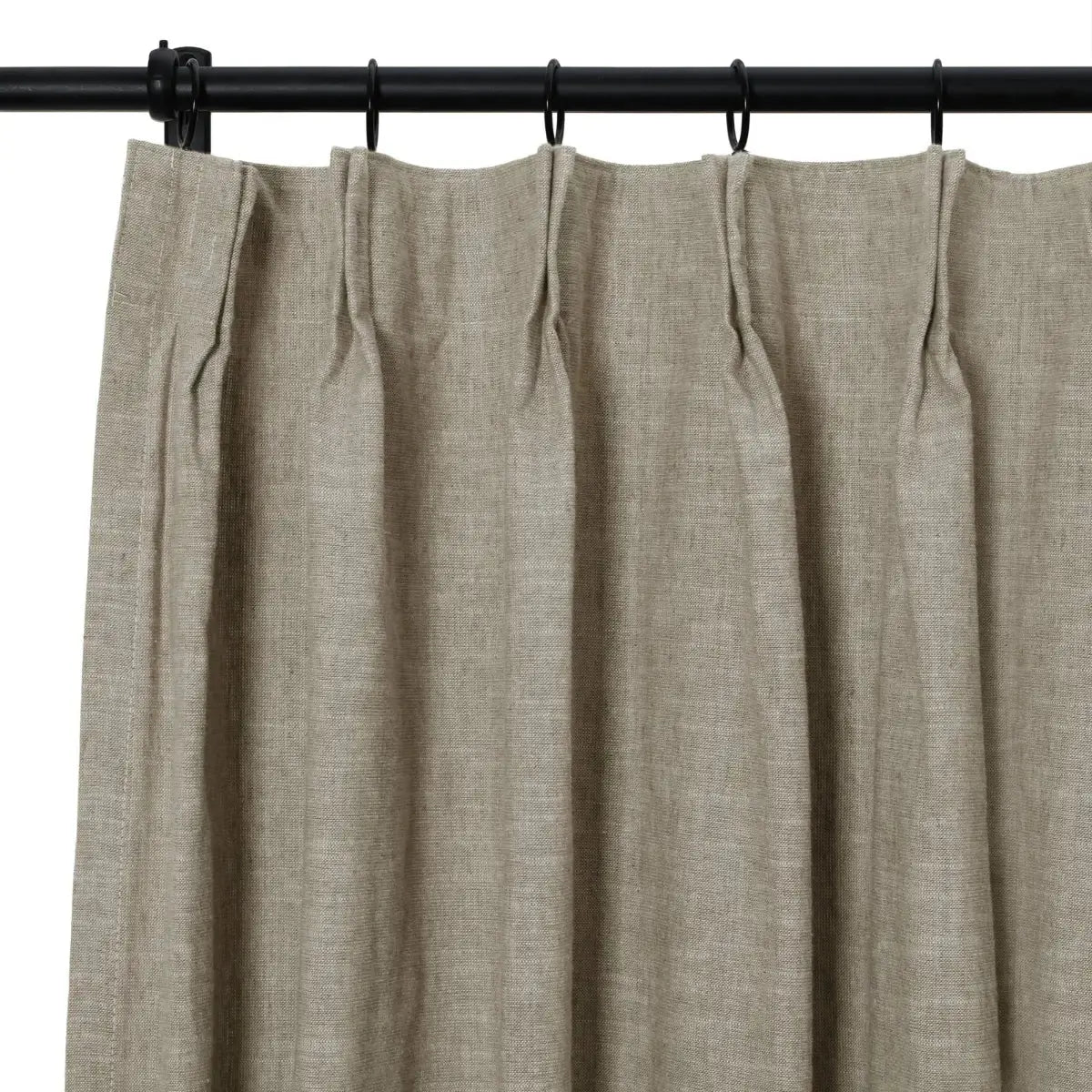 Photograph of a natural linen pinch pleat curtain in a muted beige tone hanging from a black rod with rings, showcasing its coarse textured weave