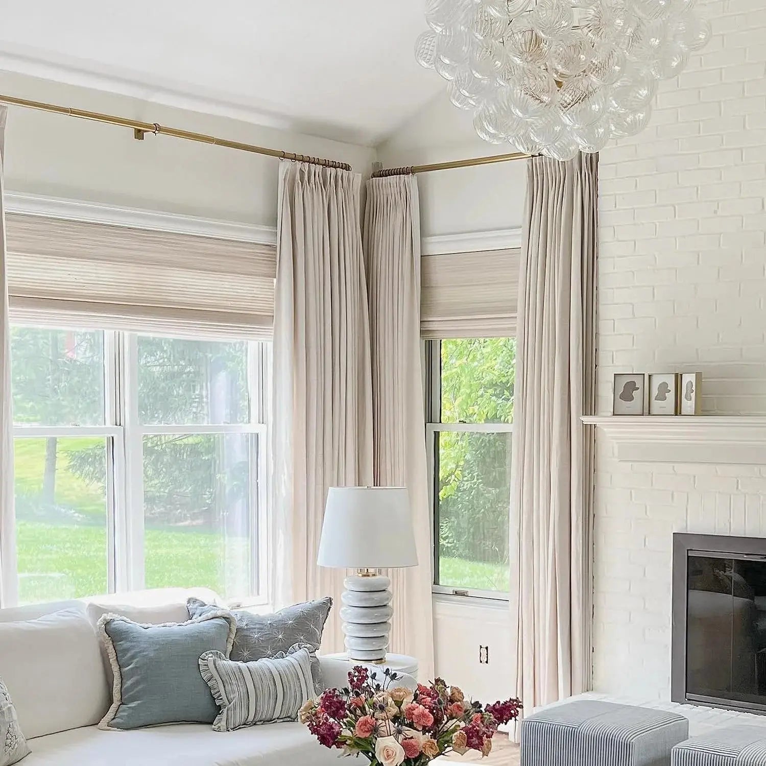 Photograph of a bright modern living room with a clear glass bubble chandelier, white brick fireplace, and a vibrant pink and burgundy floral bouquet