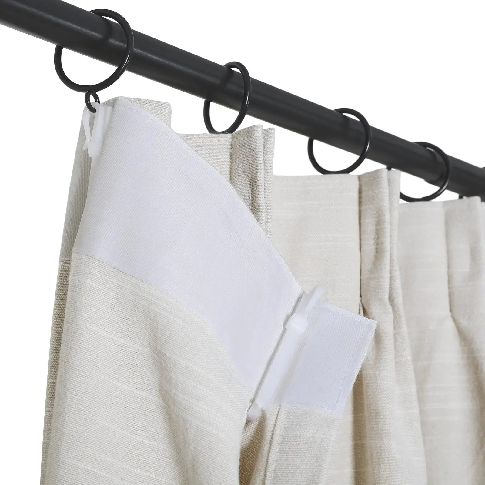 Close-up of light beige textured curtains with a white top band and soft pleats, hung on a black metal rod using black rings and white plastic clips