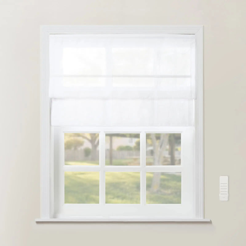 A white Roman shade covers the top half of a multi-pane window looking out onto a blurry green yard, with a white wall-mounted remote control on the adjacent beige wall