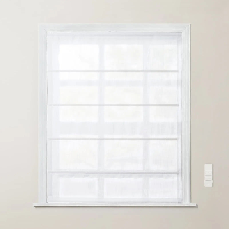 White sheer fabric Roman shade with horizontal folds fully lowered over a window with a white frame and a white wall-mounted remote control
