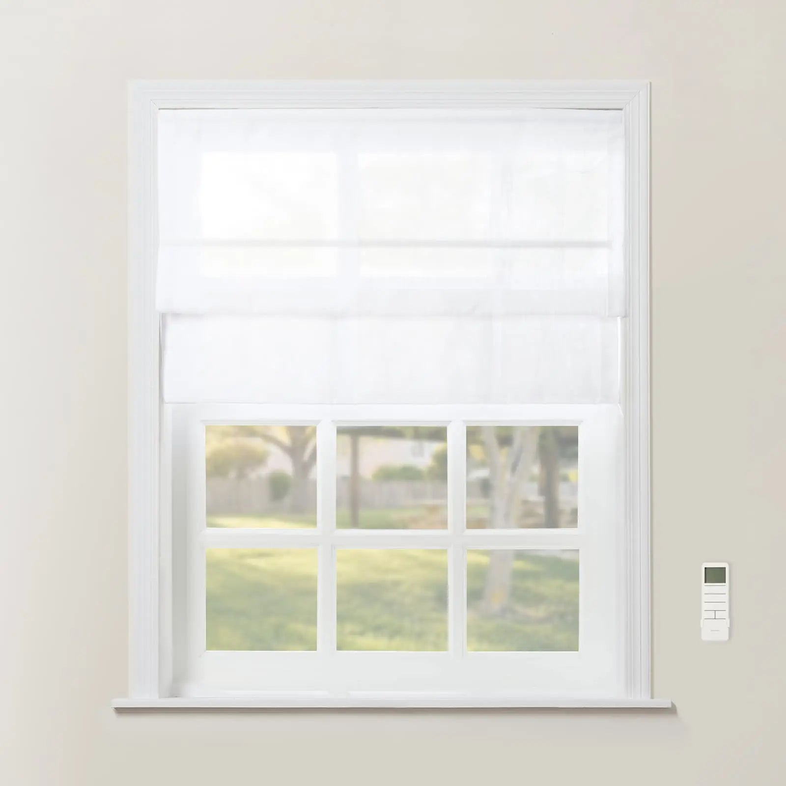 A window featuring white Roman shades over a multi-pane frame, revealing a blurred green suburban backyard, with a white remote control mounted on the light beige wall