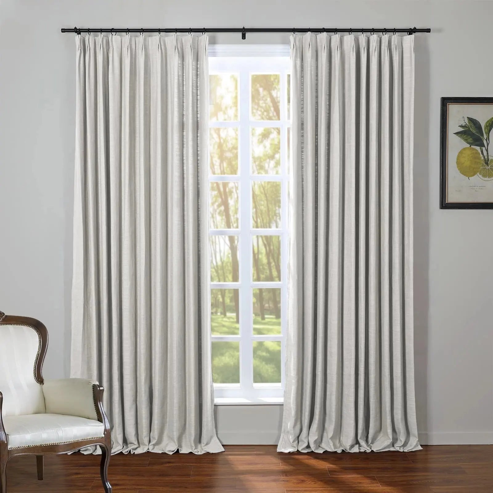 Photograph of light gray pleated curtains on a black rod framing a white multi-pane window overlooking a sunny forest, beside a classic wooden armchair with white upholstery and a framed lemon print