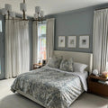 A modern bedroom showcases a white upholstered bed with a gray floral duvet and throw pillows, a striking bronze sputnik-style chandelier, and three framed botanical prints above the headboard on light gray walls