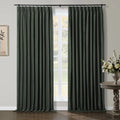 Dark green pinch-pleat curtains adorning a sunlit window in a contemporary room, featuring a carved wooden side table with a white flower arrangement and minimalist wall art